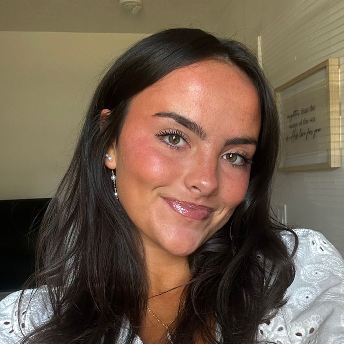 Young woman smiling indoors, representing student anonymously exposing essay details about trans instructor removal.