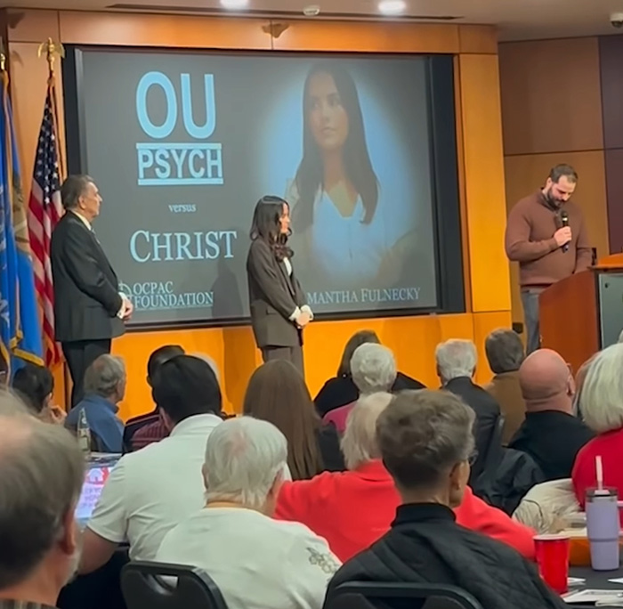 Audience listening to a speaker at a university event discussing a student essay that exposed details about a trans instructor removal.