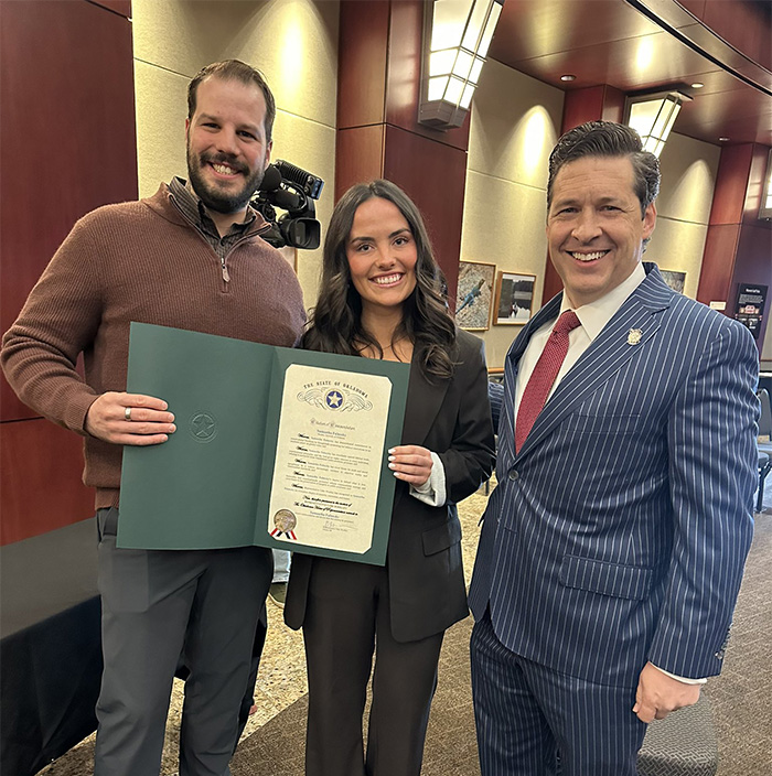 Three people smiling in a formal setting holding a certificate related to student essay exposing trans instructor removal.