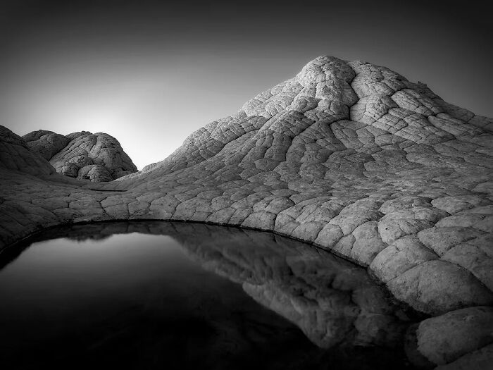 Black and white landscape featuring rocky hills and a still water reflection, showcasing best nature photography in 2025 awards.