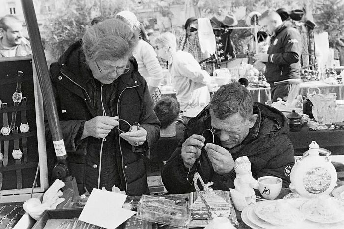 Two people examining jewelry closely at a busy market capturing street moments that feel like magic in daily life.