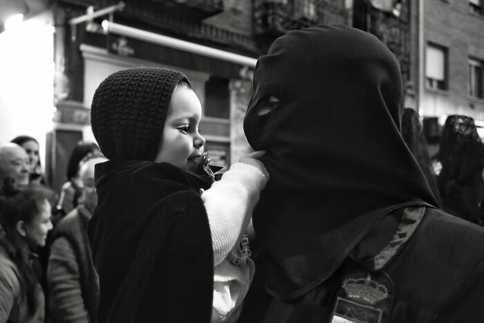 Child wearing a hood touching the face of a masked person during a magical street moment in daily life.
