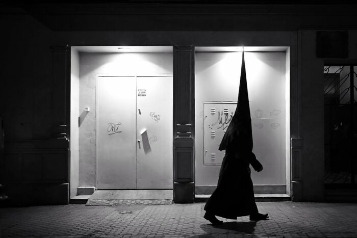 Person in traditional hooded costume walking on a street at night, capturing the marvels of daily life in a magical moment.