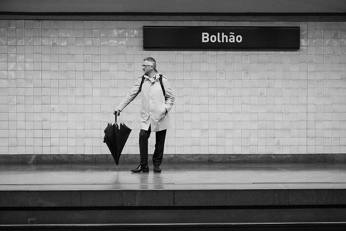 Man waiting with umbrella at Bolhão station, capturing street moments that reveal the marvels of daily life.