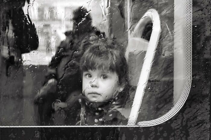 Child looking through rain-covered window on a street, capturing the marvels of daily life in a magical moment.