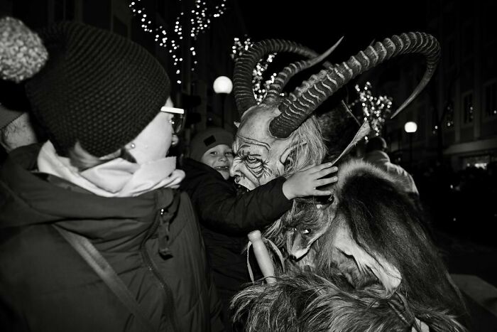 Child embracing person in a horned costume during street moments capturing the marvels of daily life magic at night.