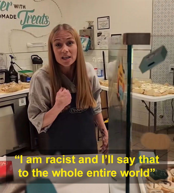 Woman in a Cinnabon apron speaking angrily behind a bakery counter during a racist tirade against a Somali couple.