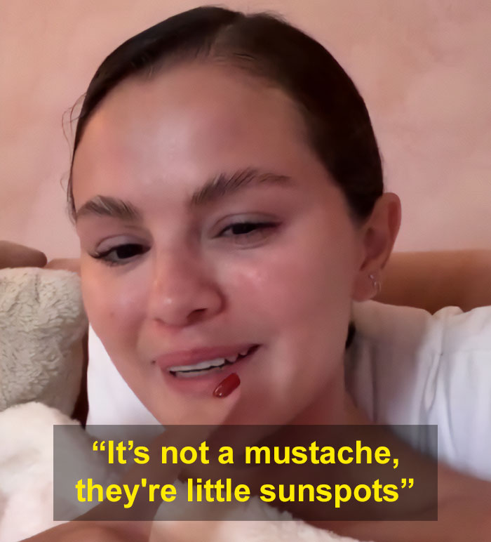 Selena Gomez responding to fan about how she shaves her mustache while smiling indoors with natural makeup.