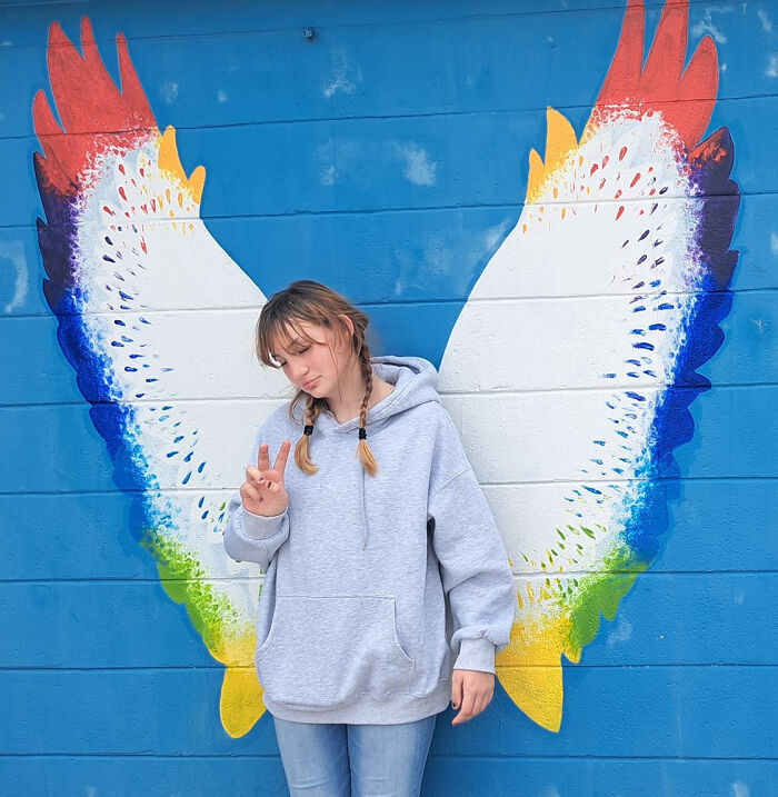 Teen girl posing in front of colorful painted wings on a blue wall symbolizing innocence before disturbing tactic incident.