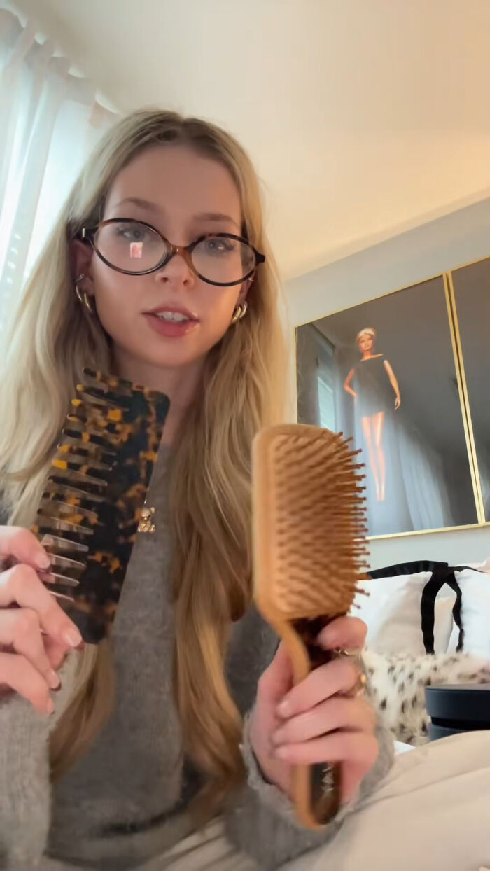Young woman with glasses holding two hairbrushes, sharing top Christmas gifts people highly recommend.