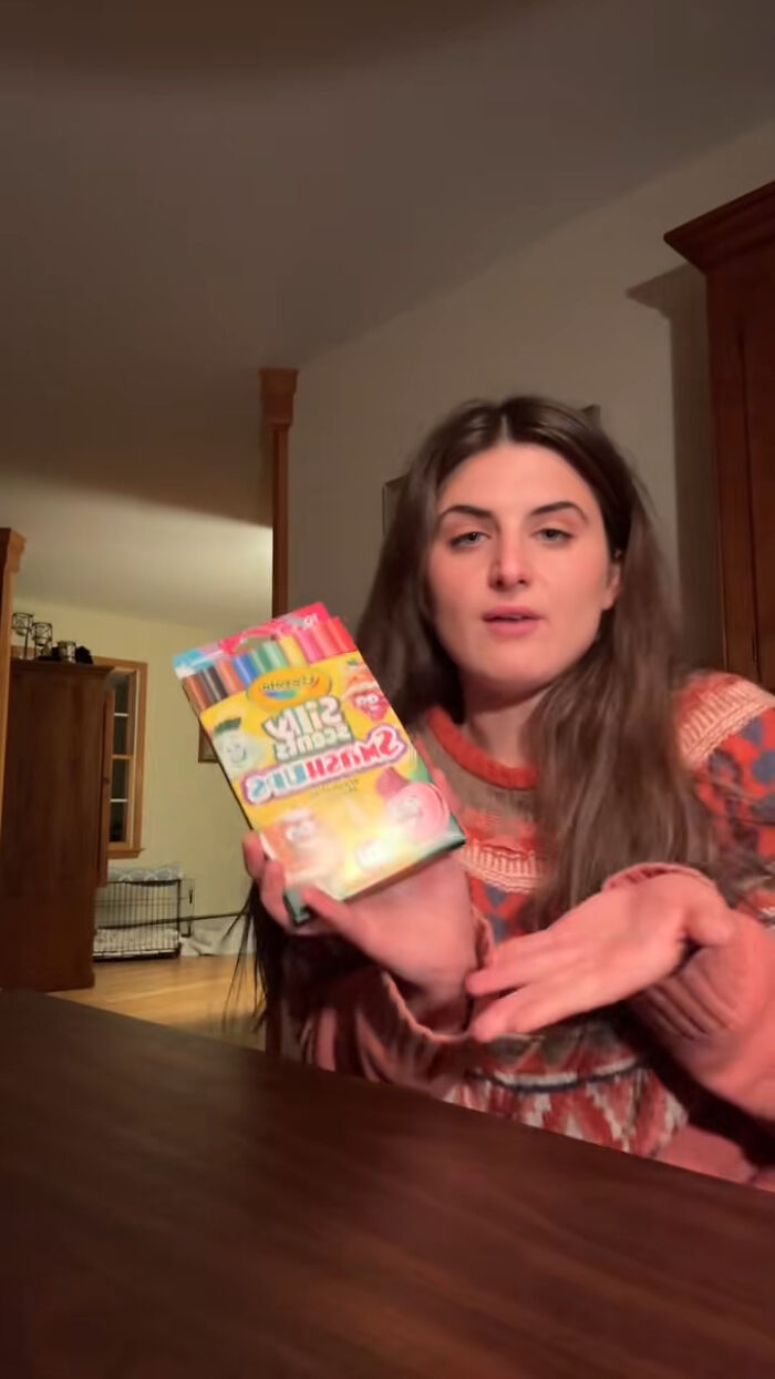 Woman holding dollar store craft markers, discussing child&rsquo;s Angel Tree haul backlash in indoor home setting.