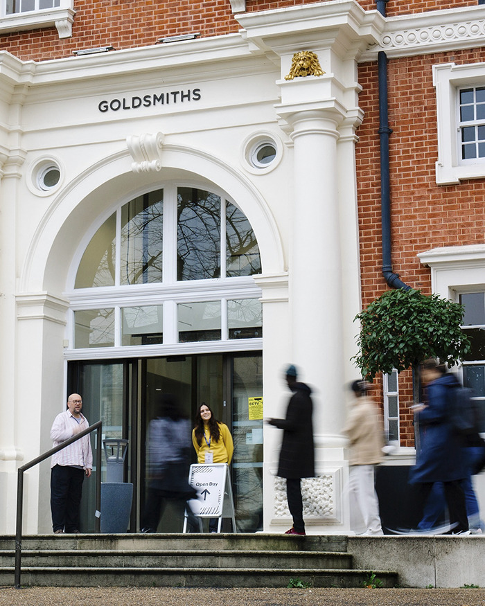 Entrance of Goldsmiths university building with students and staff outside during an open day event, highlighting wealthy US student behavior.