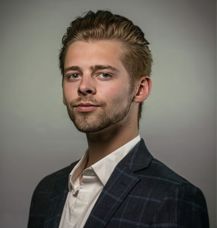 Young wealthy US student wearing a dark blazer and white shirt posing confidently against a neutral background.