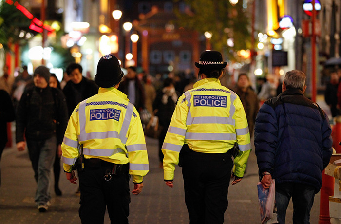 Two metropolitan police officers walking in a crowded urban area investigating wealthy US student behavior after altercation.