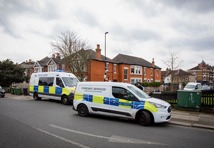 Police forensic services vehicles parked outside residential homes investigating altercation involving wealthy US student behavior.