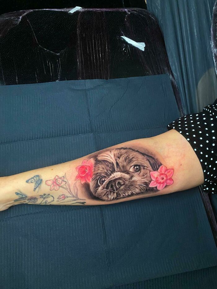 Realistic pet portrait tattoo on forearm with pink flowers, a beautiful tribute turning memories into lasting ink.