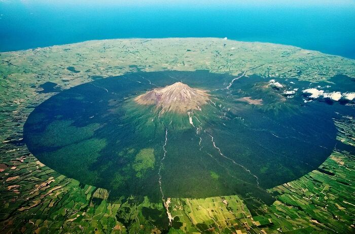 Aerial view of a massive volcanic mountain casting a large shadow, evoking fear for those with megalophobia.