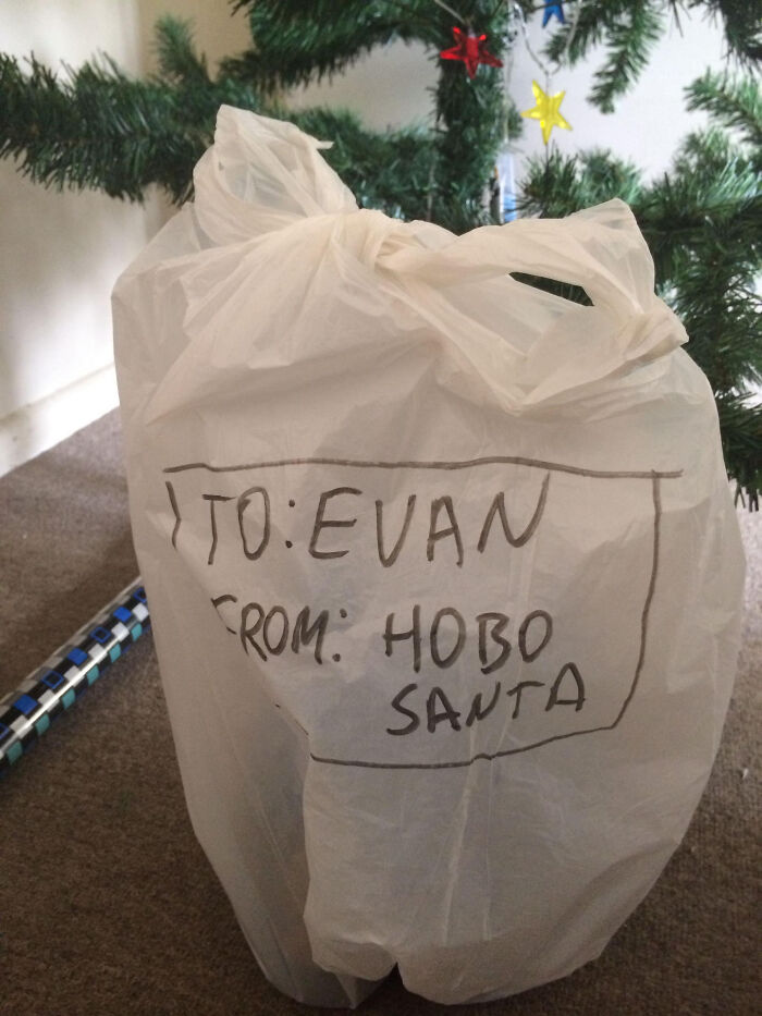 White plastic bag gift wrap labeled to Evan from Hobo Santa under a decorated Christmas tree, a funny gift wrap idea.