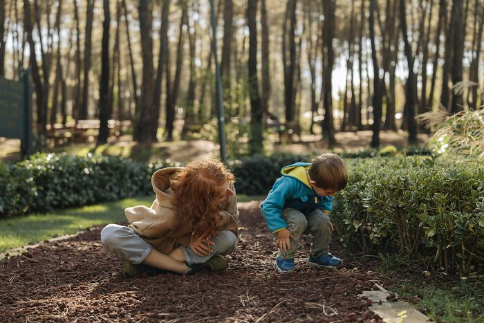 Two children exploring outdoors near bushes in a park, illustrating modern parenting trends and outdoor play.