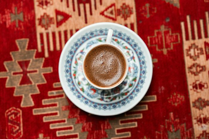 Cup of traditional Greek coffee on a decorative saucer placed on a vibrant red patterned Greek village rug