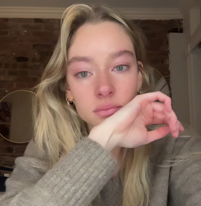 Young woman with blonde hair and a gray sweater wiping tears, related to friend of NYU shove victim viral video exposure.