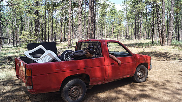 Red pickup truck loaded with miscellaneous items parked in a sunny forest illustrates culture shocks of moving to Florida from Canada.