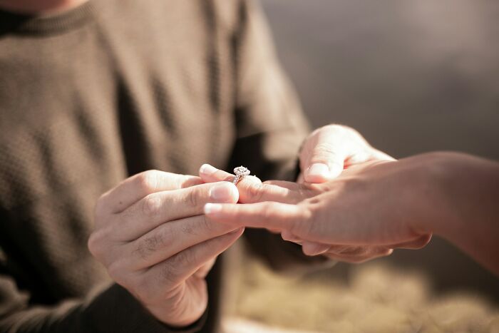 Person placing a ring on another’s finger outdoors, unrelated to funerals or funeral events.