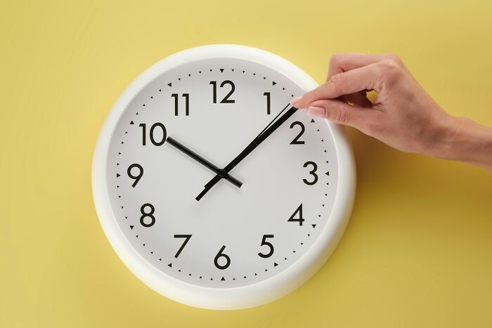 Hand adjusting a white wall clock on a yellow background illustrating surprising facts that sound made up but are true.