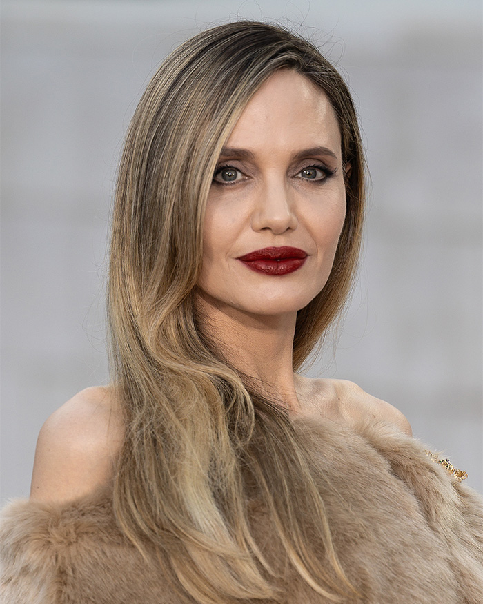Angelina Jolie in a fur coat with long hair and red lipstick clapping back at trolls over mastectomy scars.