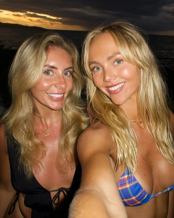 Adult stars Annie Knight and Bonnie Blue smiling for a selfie at sunset with ocean in the background.