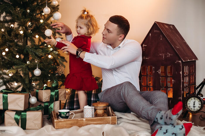 Man and child decorating Christmas tree while wife and baby are left alone, highlighting husband ditching family on Christmas.