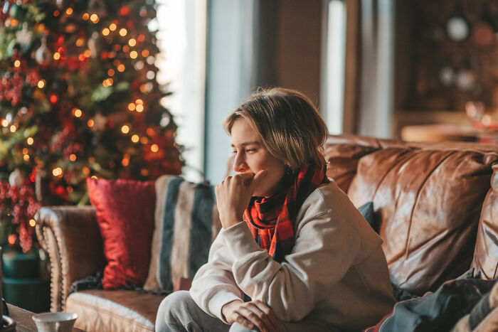 Wife heartbroken sitting alone on couch near Christmas tree with sad expression during holiday season at home