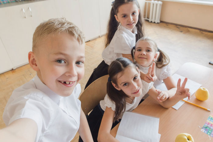 Four kids sitting at a table as one takes a selfie, illustrating family babysitting expectations and sibling dynamics.