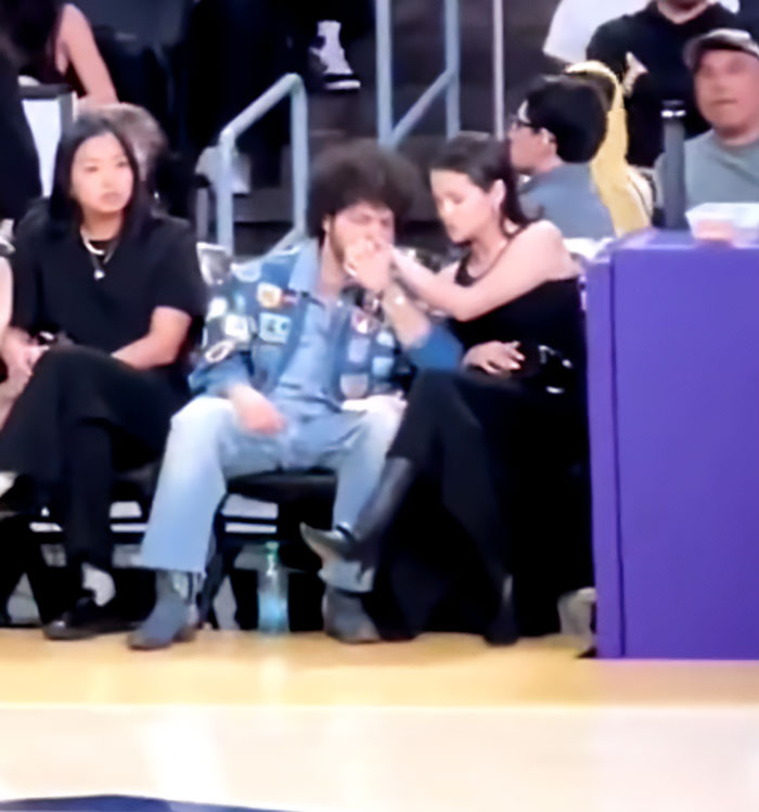 Benny Blanco and Selena Gomez sitting courtside during a game, with fans visible in the background. Benny Blanco and Selena Gomez sitting courtside during a game, with fans visible in the background.