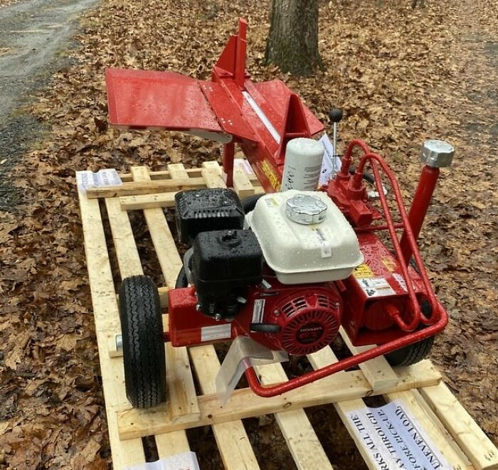 Red engine machine with black and white parts placed on a wooden pallet surrounded by fallen autumn leaves outdoors.