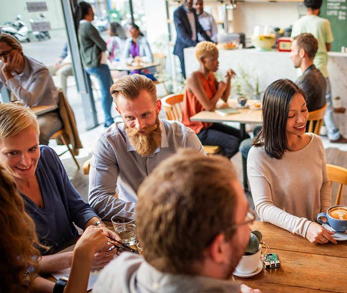 A diverse group of people sharing stories and laughing together in a bright café setting, showing chaotic good moments.