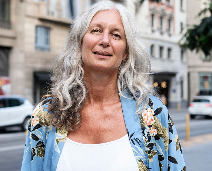 A smiling woman with long gray hair wearing a floral kimono standing on a city street sharing chaotic good moments.