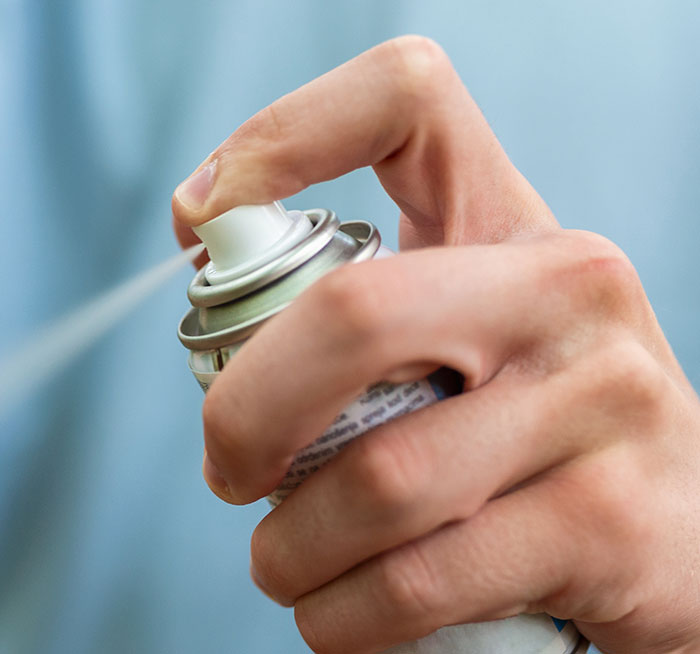 Hand pressing spray can nozzle releasing mist, illustrating chaotic good actions shared by 50 people.