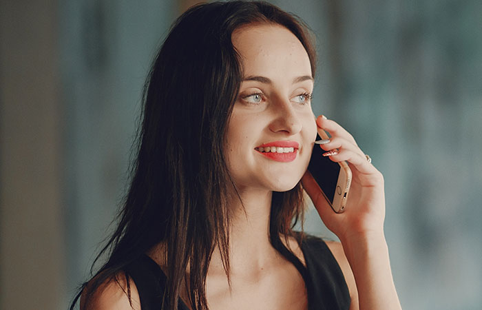 Young woman with long dark hair smiling while talking on phone, representing chaotic good moments shared by people.