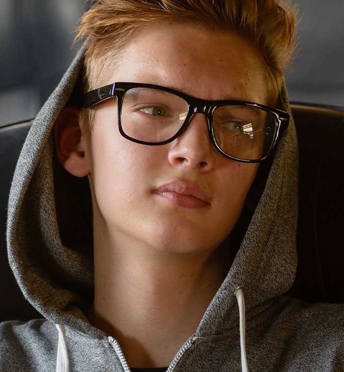 Teen wearing glasses and a gray hoodie looking thoughtfully out the window, representing chaotic good moments shared by people.