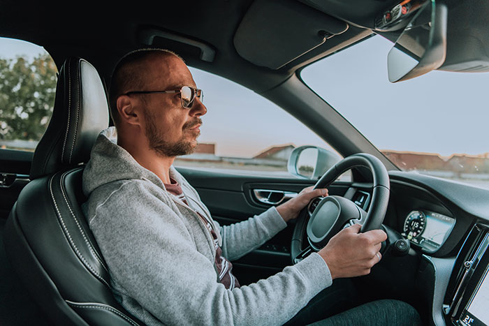 Man driving a car wearing glasses and casual clothing, representing a calm moment amidst chaotic good actions shared by people.