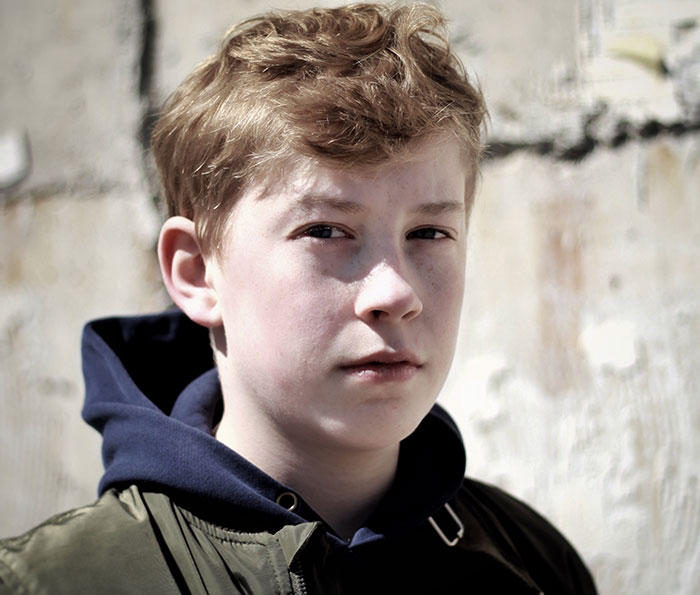 Portrait of a young boy with a serious expression, representing chaotic good moments shared by 50 people.