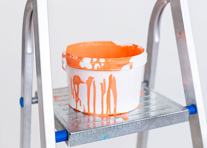 Orange paint bucket with paint drips sitting on a metal ladder revealing industry secrets from painting jobs.