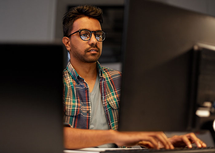 Man wearing glasses and a plaid shirt working on a computer, discovering industry secrets from his job.
