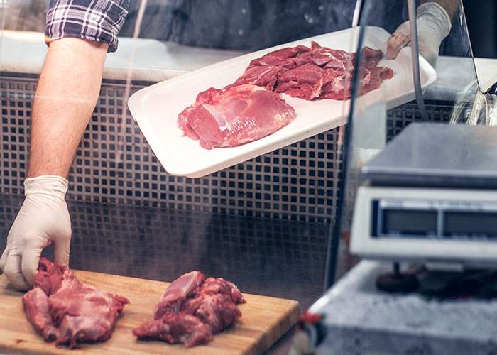 Butcher wearing gloves handling raw meat on a cutting board and tray, revealing industry secrets customers rarely know.
