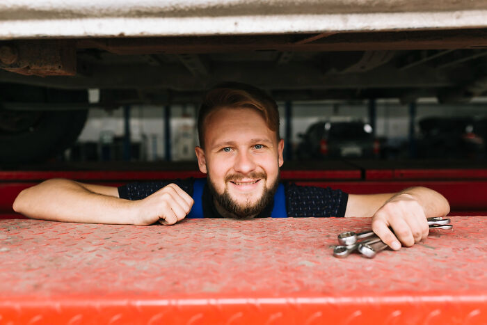 Man smiling under a car holding wrenches, illustrating the biggest bullet dodged without realizing it at the time