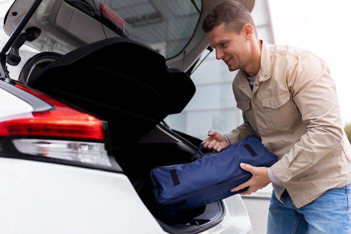 Man packing a blue bag into a car trunk, illustrating the concept of the biggest bullet dodged without realizing it.