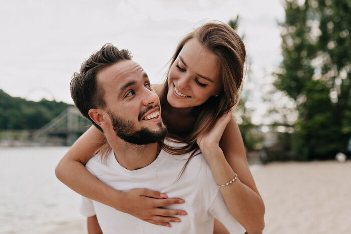 Young couple at the beach smiling and enjoying a piggyback ride, symbolizing dodging the biggest bullet in life moments.