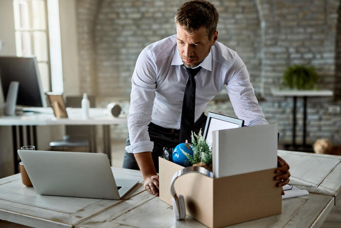 Man in office looking at box of personal items, reflecting on biggest bullet dodged without realizing it.