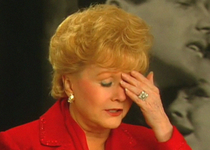 Mujer rubia con expresión de frustración y tristeza, destacando momentos de traición y backstabbing en Hollywood.